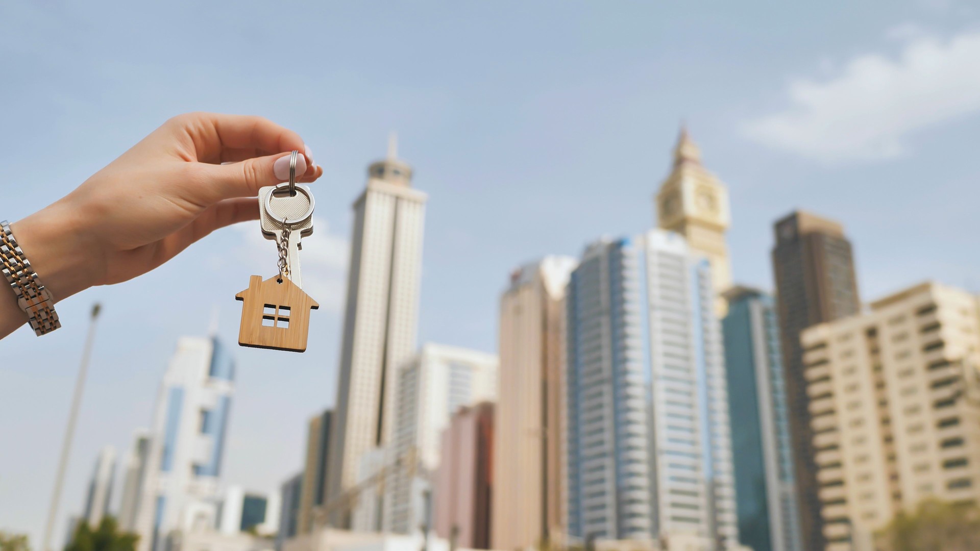 Real estate purchase concept. The girl holds the keys to a new house on the background of a Dubai skyscraper